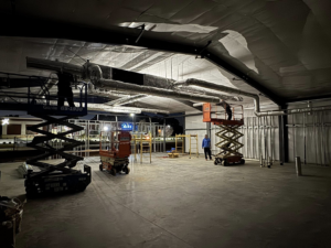 HVAC technicians installing insulated ductwork on scissor lifts at night for Delta Heating, Cooling, Plumbing in Wilson, NC.