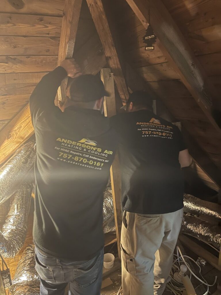 Two HVAC technicians installing or repairing ductwork in an attic for Anderson's Air in Newport News, VA