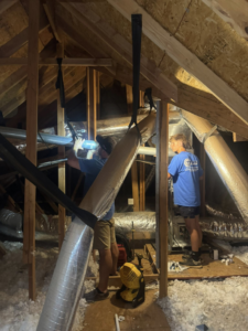 Two HVAC technicians from Thomas Mechanical Services Corp installing ductwork in an attic in Edmond, OK.