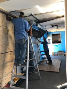 HVAC technicians installing a large ductwork component or ventilation hood at a job site for Carlsbad Heating & Cooling in Carlsbad, NM.