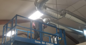 HVAC technicians installing large metal ductwork from a scissor lift for Hartwig Heating in Marshalltown, IA