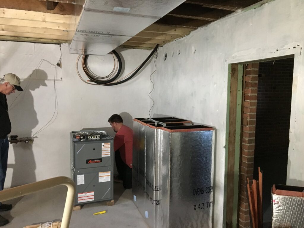 Two Prime Home HVAC technicians installing a new furnace and ductwork in a residential basement in York, PA.