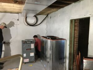 Two Prime Home HVAC technicians installing a new furnace and ductwork in a residential basement in York, PA.