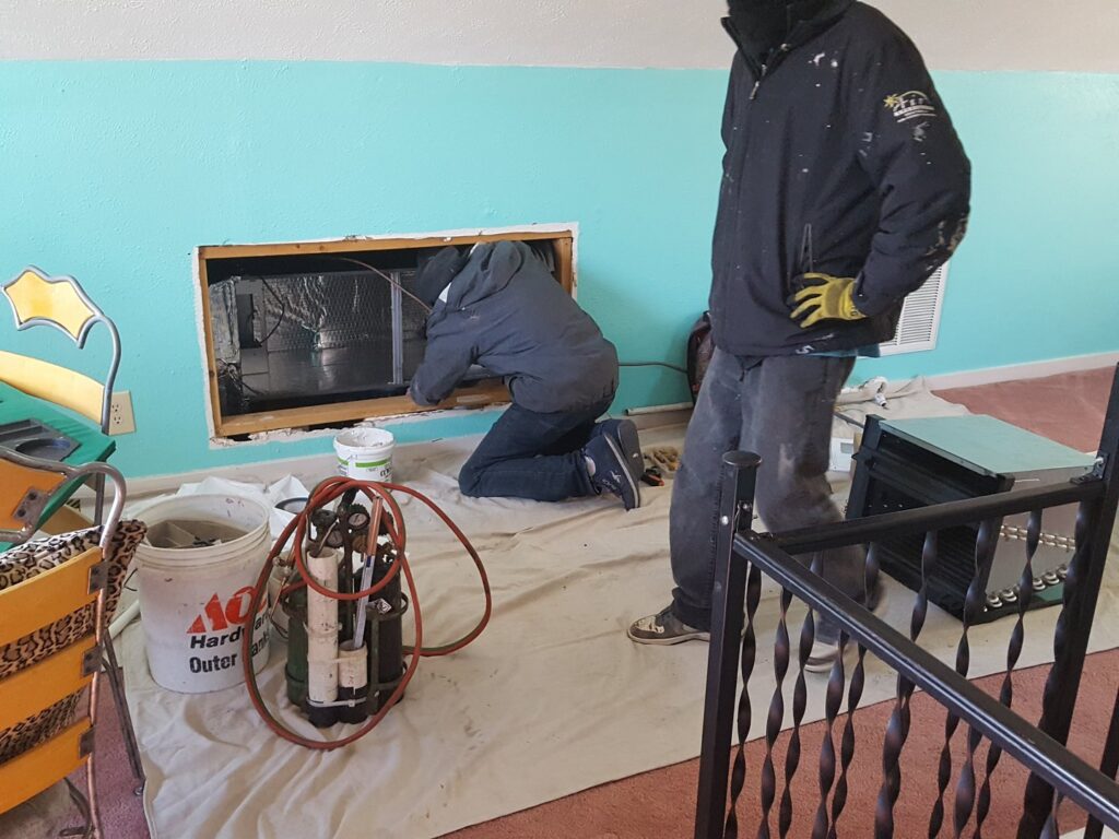 Two Air Specialty Heating & Air Conditioning technicians installing an indoor HVAC unit in a wall opening in Norfolk, VA.