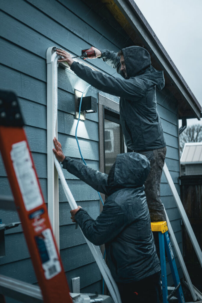 Two HVAC technicians installing line set covers on a home exterior for Elevate Heating & Cooling in Hillsboro, OR.