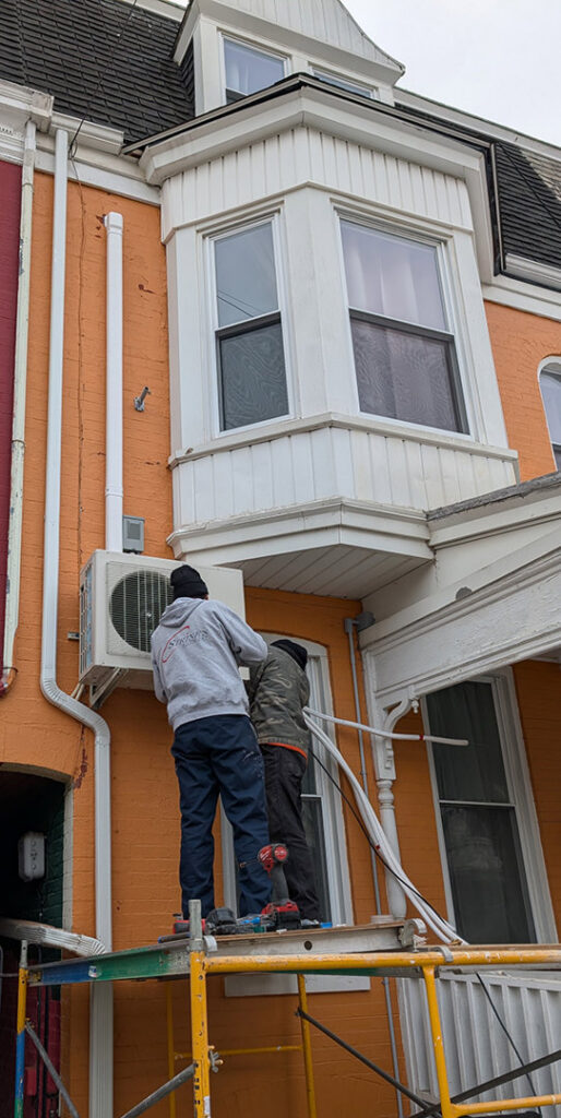 HVAC technicians installing an outdoor mini-split condenser unit on a building for Strine's Heating & A/C in York, PA.