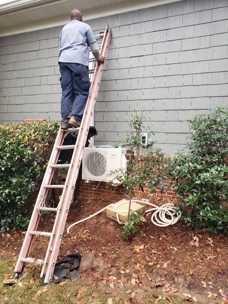 Two HVAC technicians installing an outdoor mini-split unit on a ladder for Stoudenmire Heating & Air Conditioning in Columbia, SC.