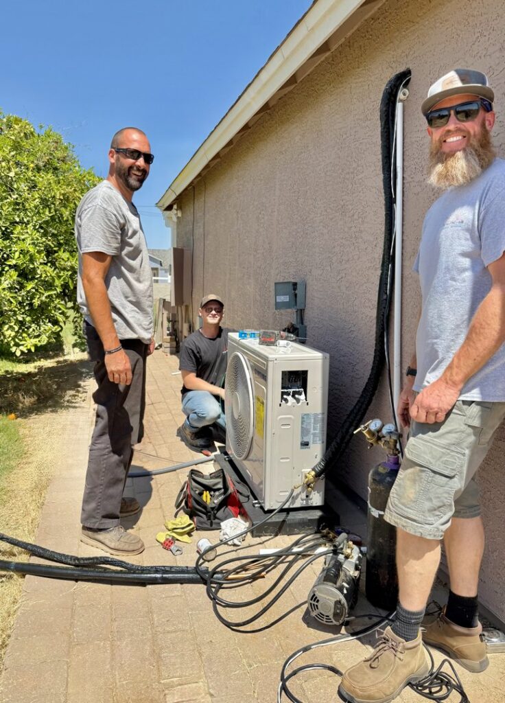 Three HVAC technicians from TK Heating and Air, PLLC installing or servicing an outdoor mini-split unit in Queen Creek, AZ