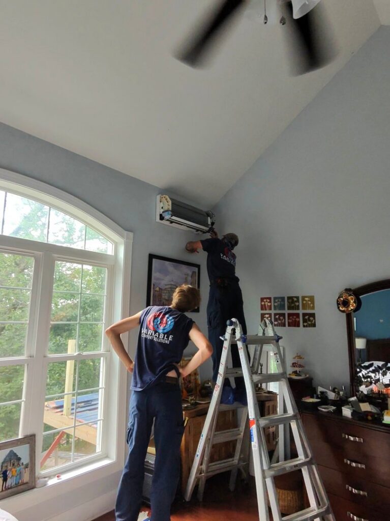 Two HVAC technicians installing an indoor mini-split unit in a bedroom for Variable Comfort Solutions in Huntington, WV.