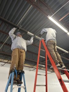 Two A&E Heating & Cooling technicians installing overhead piping in a commercial building in Fort Worth, TX.