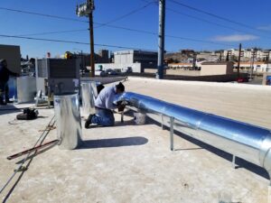 HVAC technicians installing large metal ductwork on a commercial rooftop for One Way Heating And Cooling, LLC in Horizon City, TX.