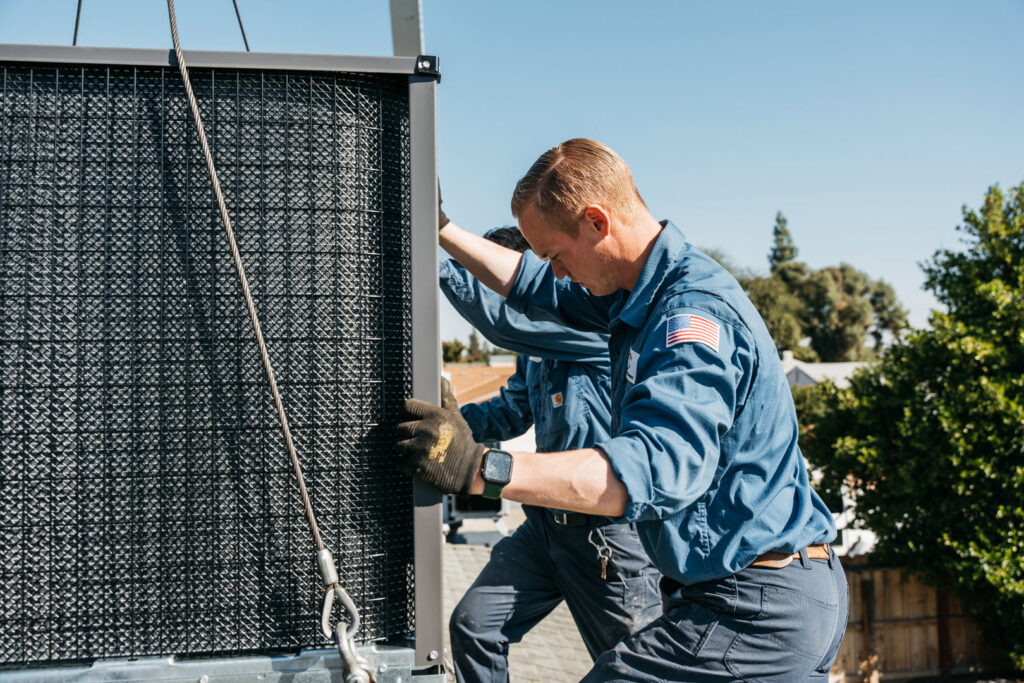 Two HVAC technicians installing a large rooftop unit for Controlled Climates Heating and Air Conditioning, Inc. in Fresno, CA.