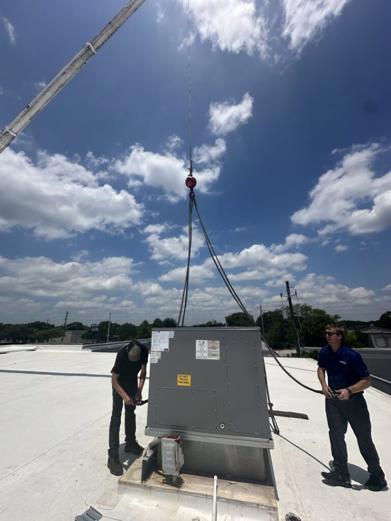 Two HVAC technicians installing a new commercial rooftop unit with a crane for Whitleys Heating and Air in Jacksonville, FL.