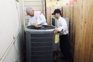 Two HVAC technicians moving an outdoor AC unit for installation or replacement by Controlled Climates Heating and Air Conditioning, Inc. in Fresno, CA.