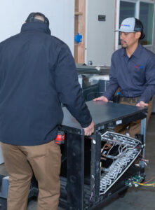 Airmech Heating and Air Conditioning technicians moving an indoor HVAC unit on a dolly in Elk Grove, CA.