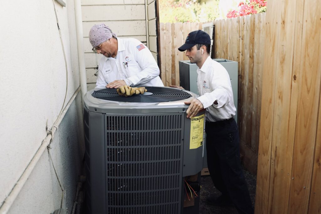 Two HVAC technicians moving an outdoor air conditioning unit for installation or removal by Controlled Climates Heating and Air Conditioning, Inc. in Fresno, CA.
