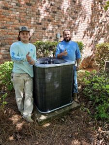 Two HVAC technicians giving thumbs up next to a newly installed outdoor AC unit by Faith Heat and Cool in West Monroe, LA