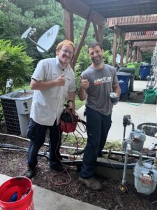 Two HVAC technicians giving thumbs up on a job site with outdoor units by Delta Heating, Cooling, Plumbing in Wilson, NC.