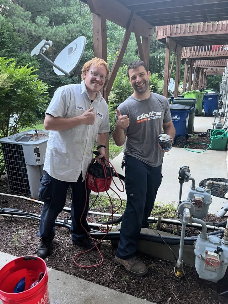 Two HVAC technicians giving thumbs up on a job site with outdoor units by Delta Heating, Cooling, Plumbing in Wilson, NC.