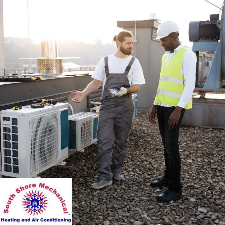 Two HVAC technicians discussing work on a commercial rooftop with multiple units for South Shore Mechanical in Abington, MA