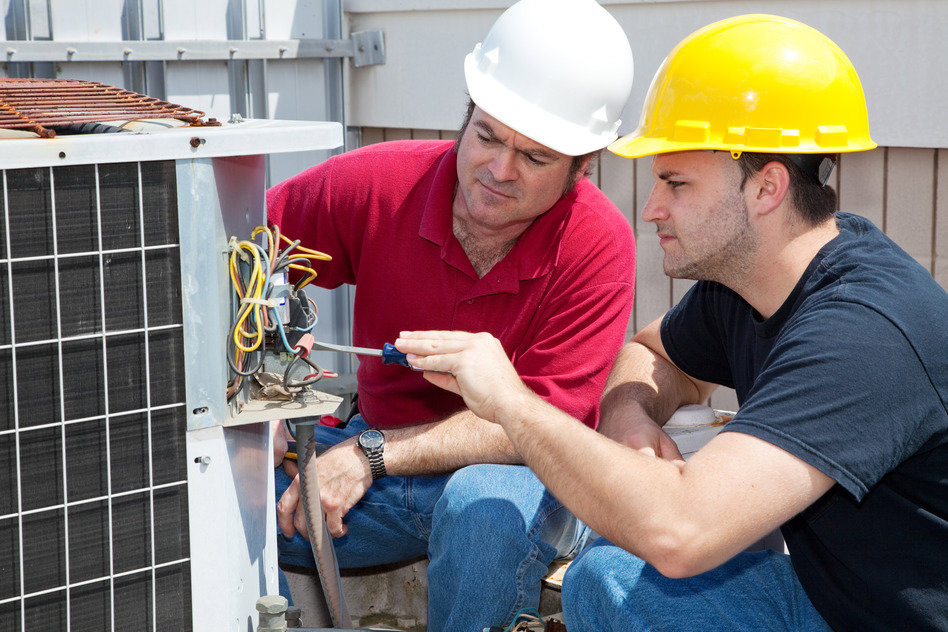 Two HVAC technicians in hard hats repairing an outdoor air conditioning unit for Trenary Service Company in Martinsburg, WV.