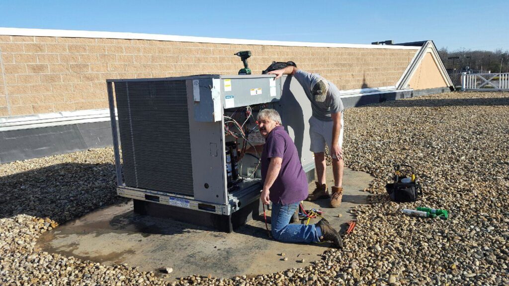 Two HVAC technicians repairing a commercial rooftop unit for Allwaysthere Heating and Cooling in Frederick, MD