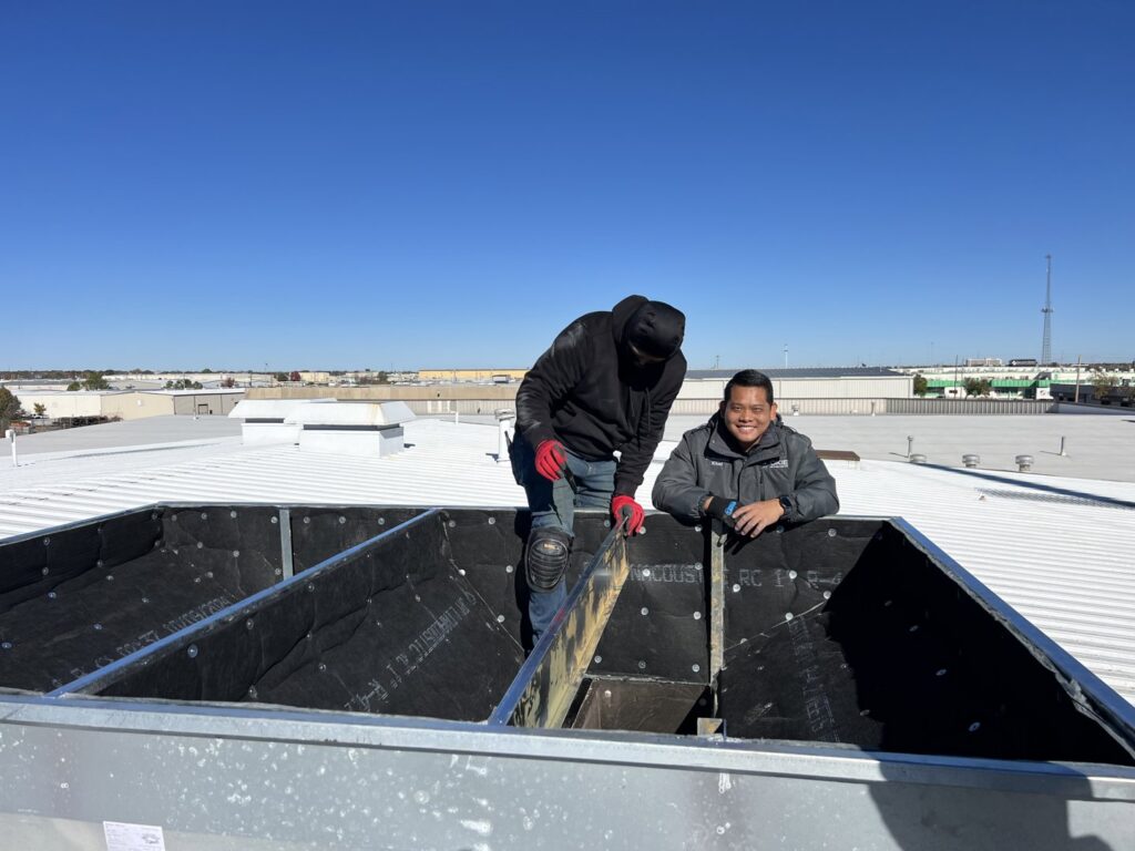Two HVAC technicians inspecting a rooftop ventilation system for OKIE Heating and Cooling in Tulsa, OK.
