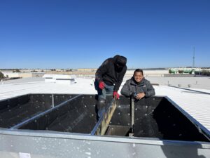 Two HVAC technicians inspecting a rooftop ventilation system for OKIE Heating and Cooling in Tulsa, OK.
