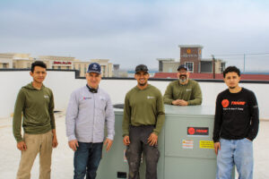 HVAC technicians standing with a large commercial rooftop unit, representing Texas Air & Heat in Arlington, TX.