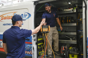 Two HVAC technicians exchanging tools from a service van, ready for a job with Swiss Air Heating & Cooling in O'Fallon, MO.