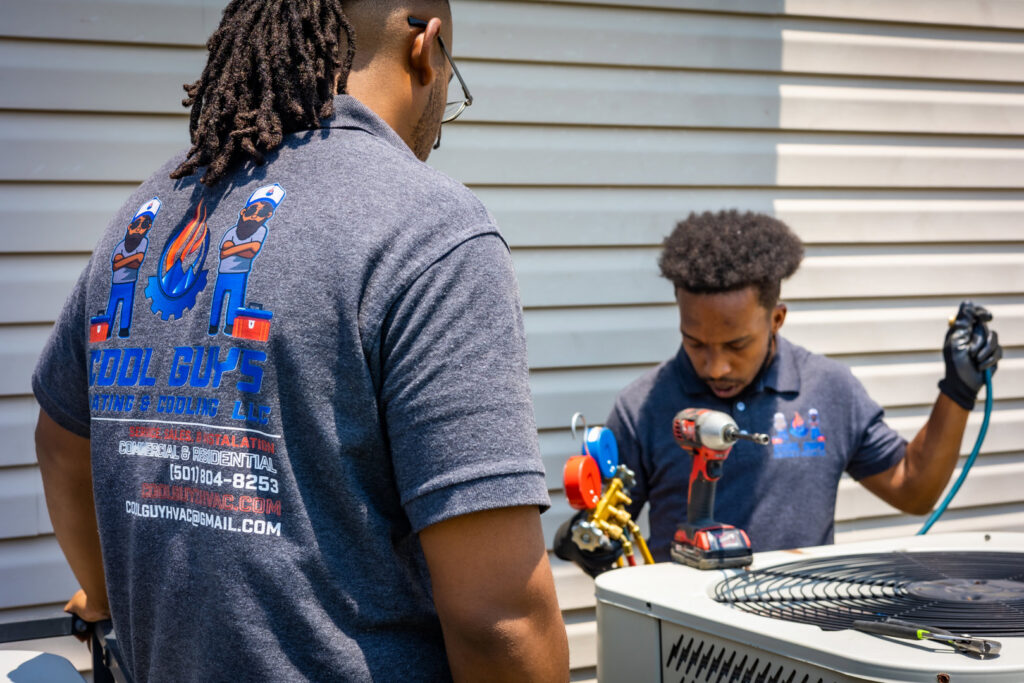 Two HVAC technicians from Cool Guys Heating & Air LLC servicing an outdoor AC unit in North Little Rock, AR.