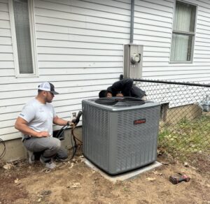 Two HVAC technicians from JCL Heating and Cooling LLC servicing an outdoor AC unit in Gresham, OR.