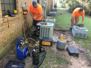 HVAC technicians servicing outdoor AC units with tools and refrigerant tanks for Cooler Solutions LLC Heating & Air in Gulfport, MS.