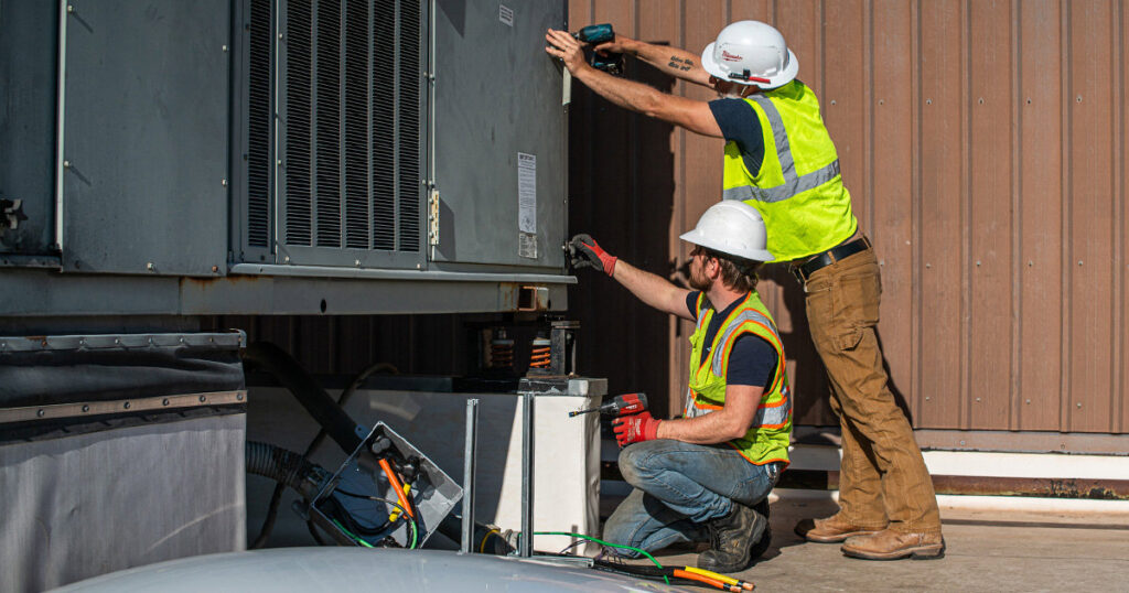 Two HVAC technicians from DMC Service, Inc. servicing a large outdoor commercial HVAC unit in Olathe, KS.