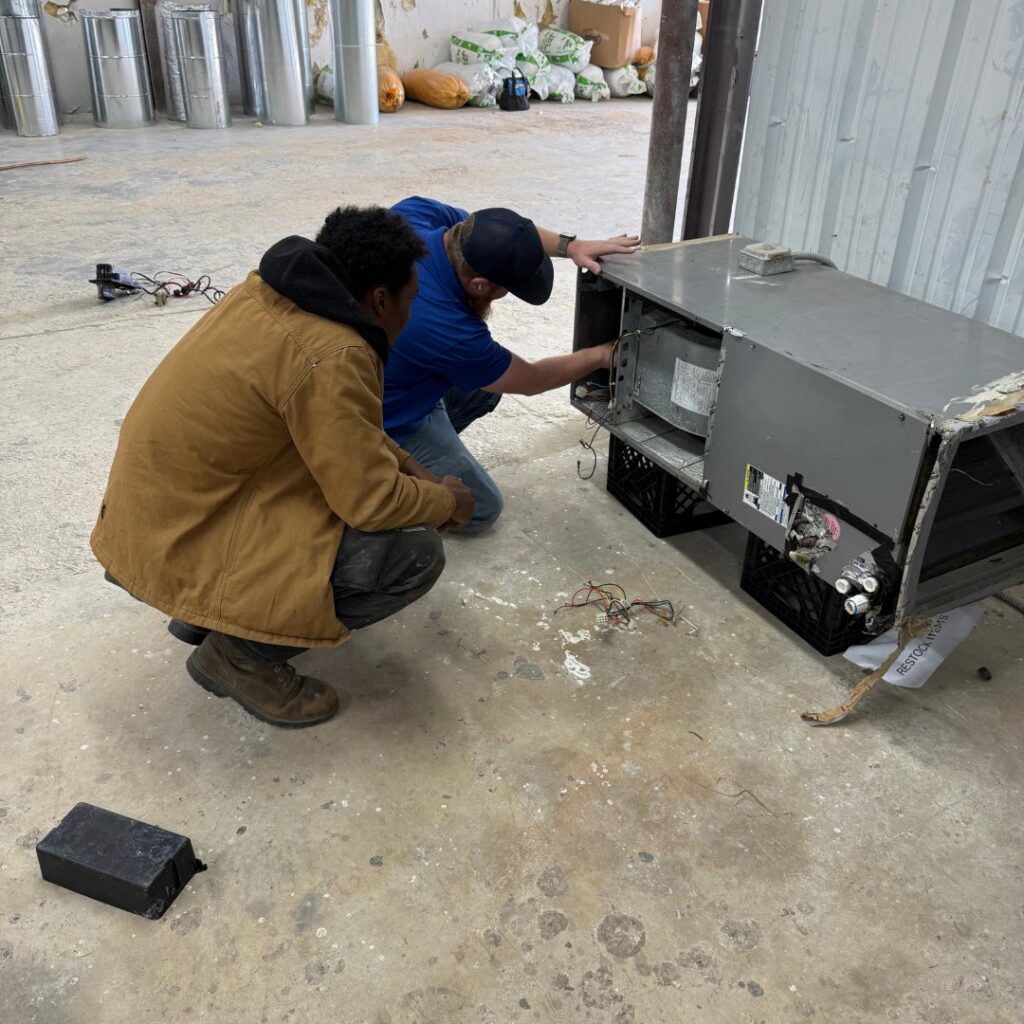 Two HVAC technicians from T & T HVAC servicing an indoor air handler or furnace unit in Amherst, OH.