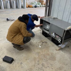 Two HVAC technicians from T & T HVAC servicing an indoor air handler or furnace unit in Amherst, OH.