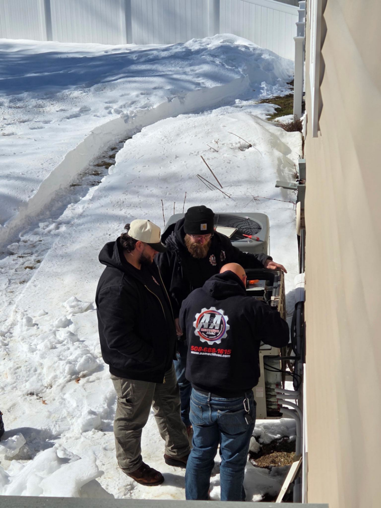 HVAC technicians from A&A Mechanical HVAC servicing an outdoor unit in the snow in Raynham, MA.