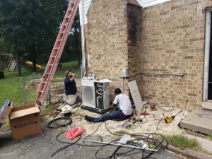 Two HVAC technicians servicing an outdoor unit next to a brick house for Air Energy Solutions in North Chesterfield, VA