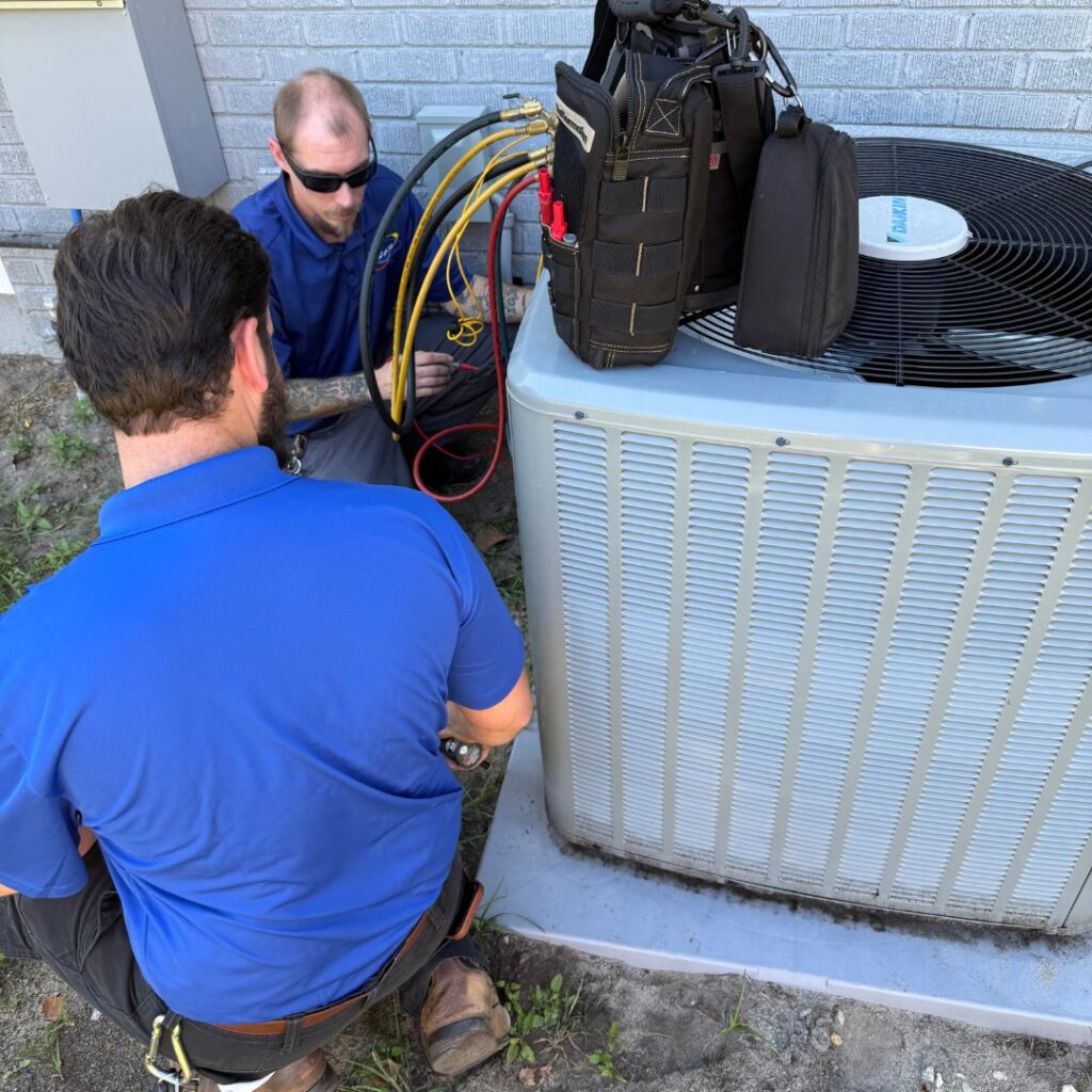 Two HVAC technicians from T & T HVAC servicing an outdoor unit, connecting gauges for diagnostics in Amherst, OH.