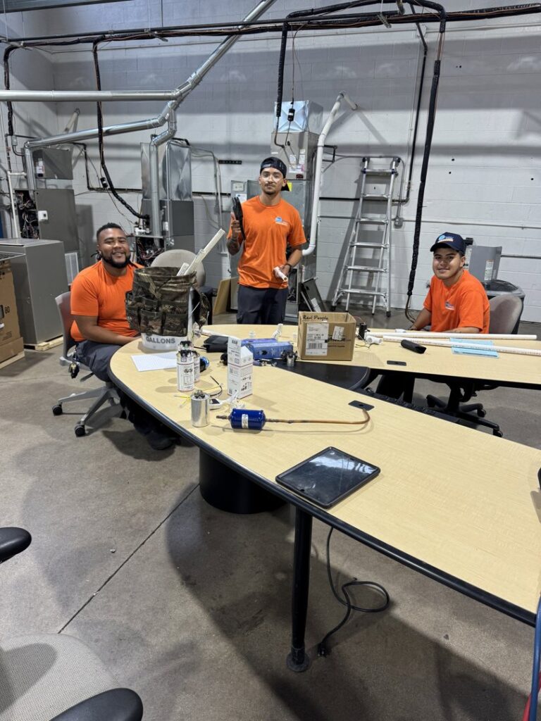 Three HVAC technicians from Deljo Heating, Cooling & Plumbing in a workshop setting, possibly training or preparing equipment in Chicago, IL.