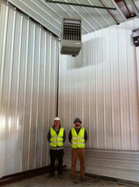 Two HVAC technicians in safety vests standing with a large overhead heating unit in a commercial building, installed by KATS Heating & Cooling in La Grange Park, IL.