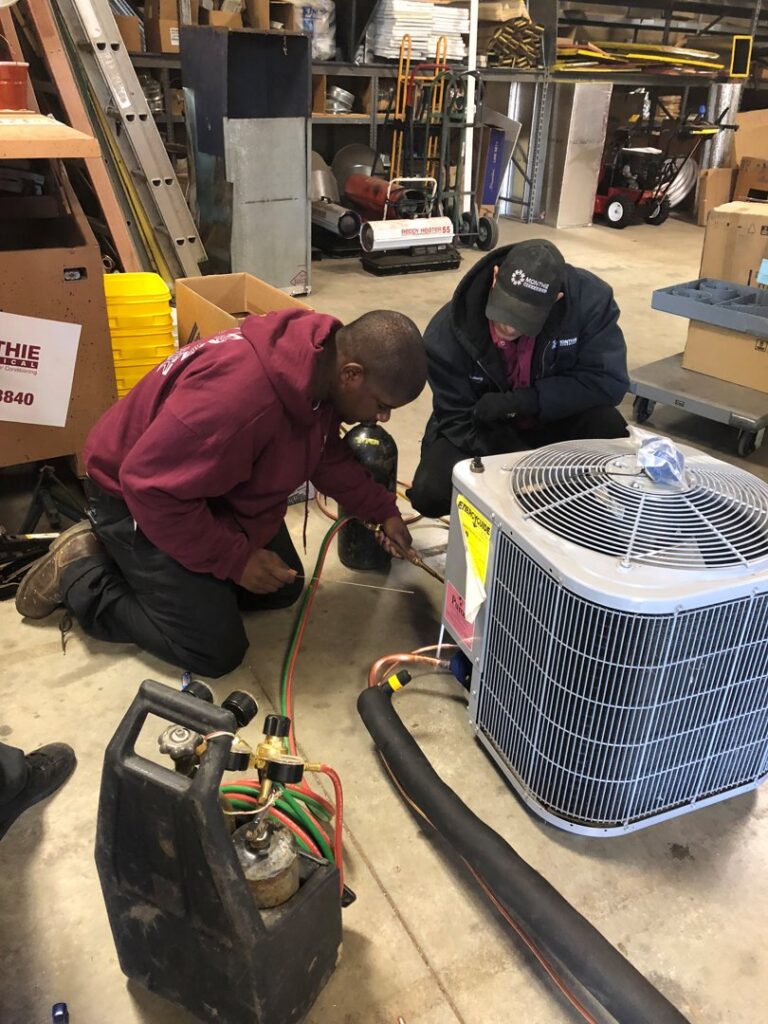 Two HVAC technicians performing work on an outdoor AC unit with welding equipment for MMI Climate Solutions in Lexington, KY.