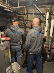 Two HVAC technicians from Unified Home Solutions working on a boiler or water heater system in Stamford, CT.