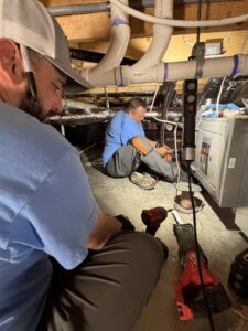 Two HVAC technicians working on ductwork and pipes in a crawl space for Wright Way Air in Streamwood, IL