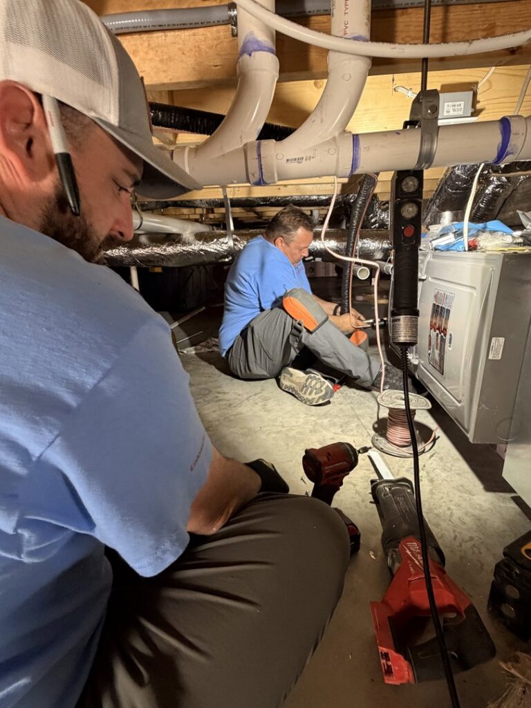 Two HVAC technicians working on ductwork and pipes in a crawl space for Wright Way Air in Streamwood, IL