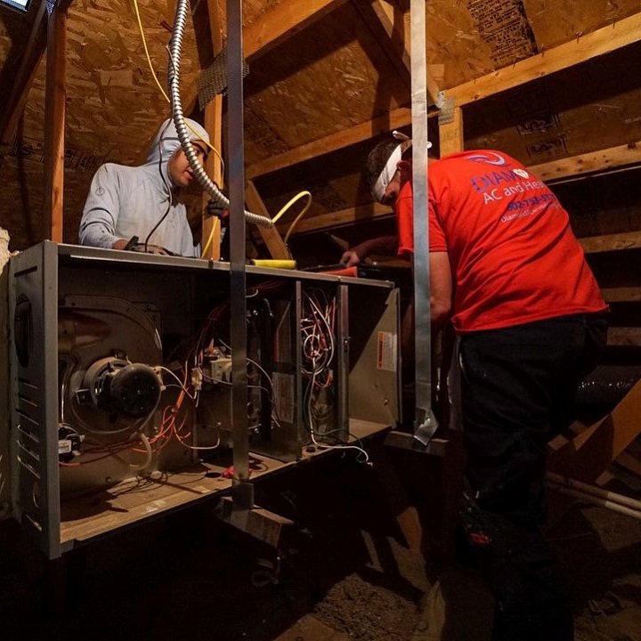 Two HVAC technicians working on a furnace or air handler in an attic for Diamond AC and Heating in Phoenix, AZ.
