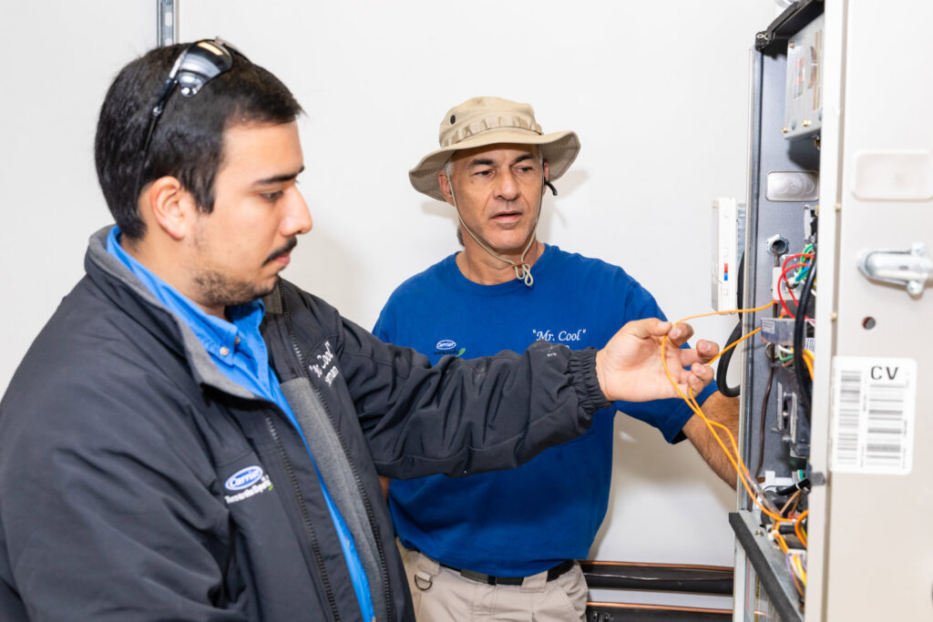 Two HVAC technicians from Mr. Cool HVAC working on the wiring inside a furnace or air handler unit in Cypress, TX.