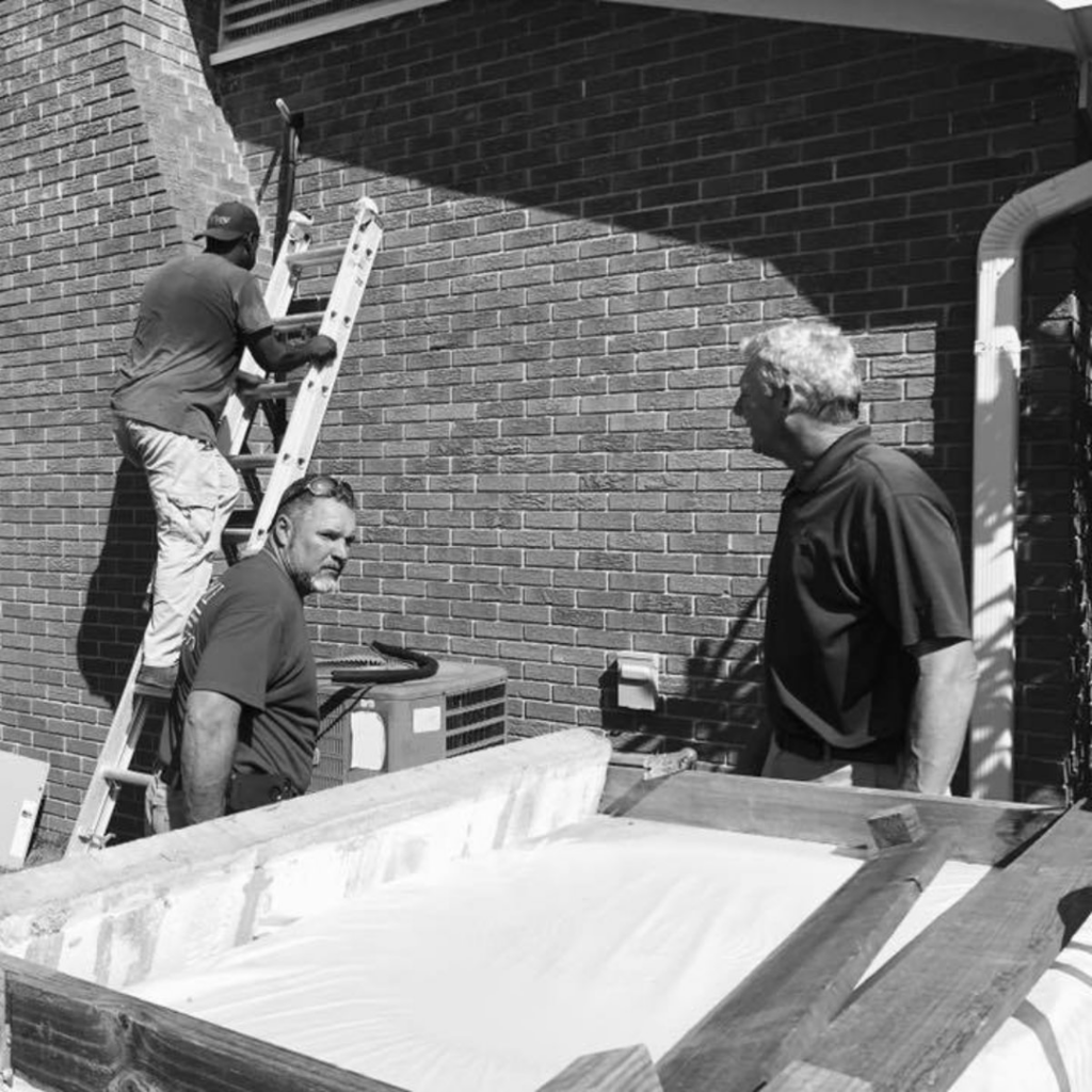 HVAC technicians working on an outdoor unit next to a brick building, provided by Hutcheson Mechanical & Exteriors in Columbia, SC.