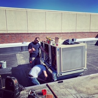 Two HVAC technicians working on a large rooftop unit for Thurston Heating and Air Inc. in Kearney, NE