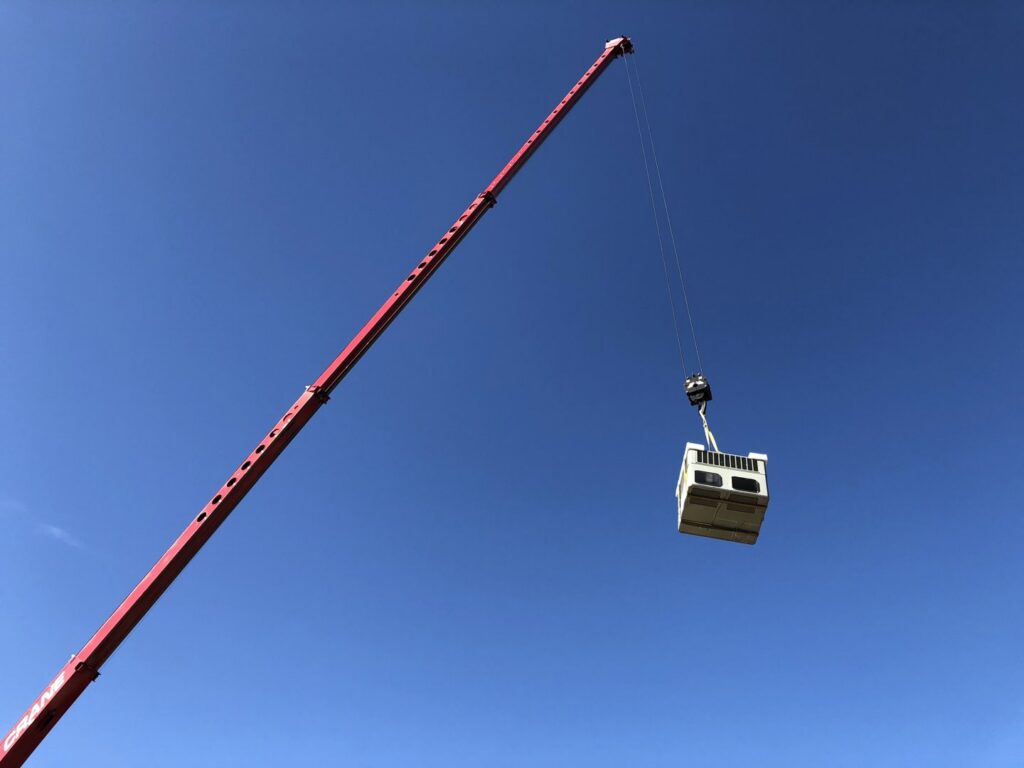 An HVAC unit being carefully lifted by a crane against a clear blue sky by Hellerud Air in Peoria, AZ.